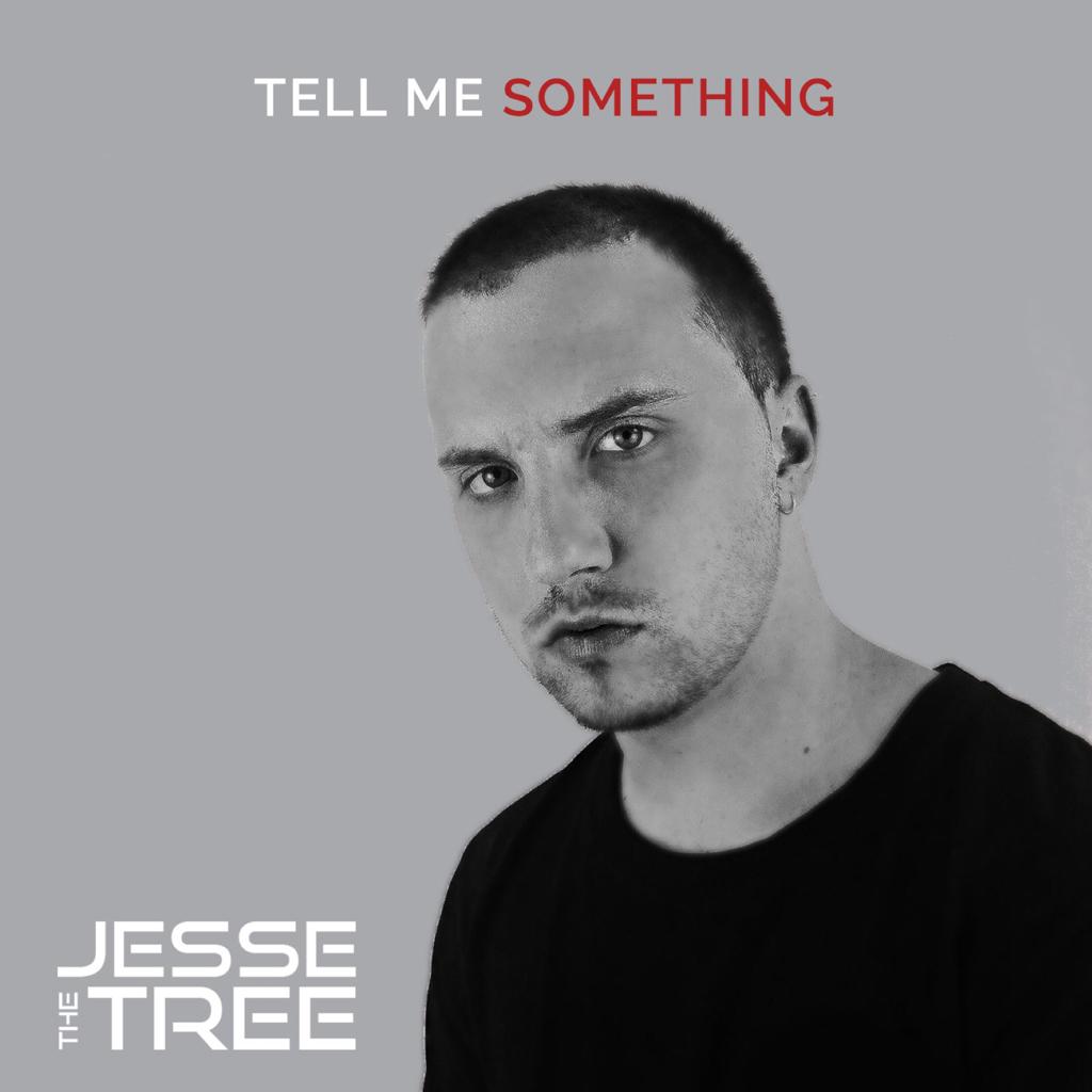 Black and white portrait of a young man with short dark hair, wearing a black shirt, looking directly at the camera with a serious expression. The background is grey, and the text 'TELL ME SOMETHING' is in red above him, while 'JESSE THE TREE' is displayed in white at the bottom.